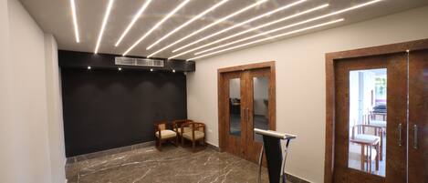 A modern lobby with a marble floor, wooden chairs, a podium, and a black accent wall.