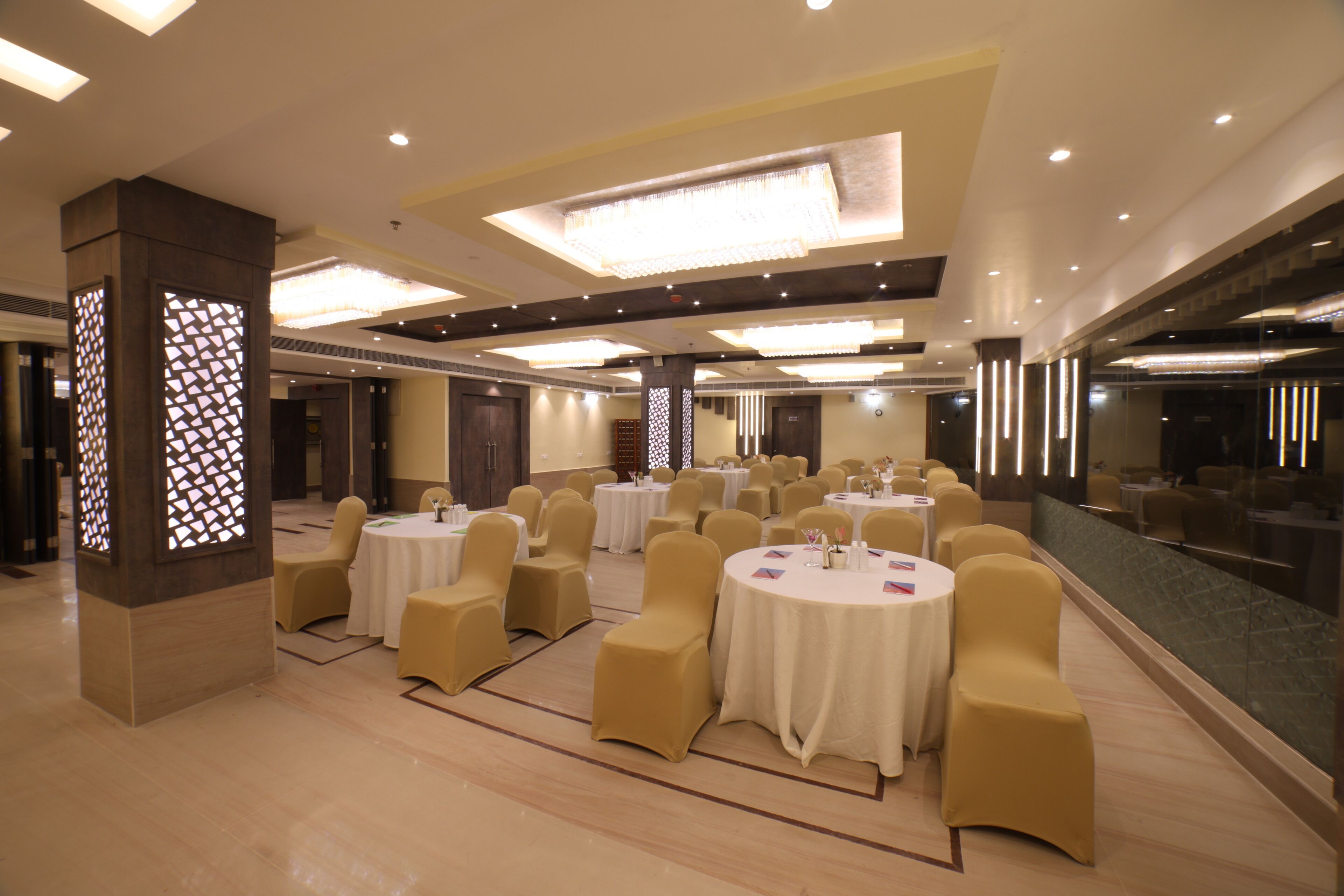 Un amplio salón de banquetes con mesas y sillas redondas, un pilar decorativo y un espejo grande que refleja la sala.