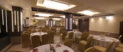 A conference room with multiple round tables, beige chairs, and modern lighting fixtures.