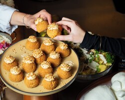 Prato de profiteroles com cobertura cremosa e nozes, segurado por uma pessoa.