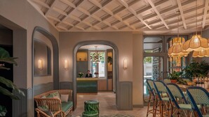 A hotel lobby with a reception desk, seating area with wicker chairs, a patterned rug, and a bar area with high stools. - Miss Fuller (Paris)
