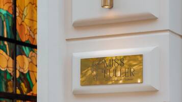 A wall-mounted light fixture and a brass plaque with the name "Miss Fuller" and "Hotel Bar Restaurant" on a white wall.