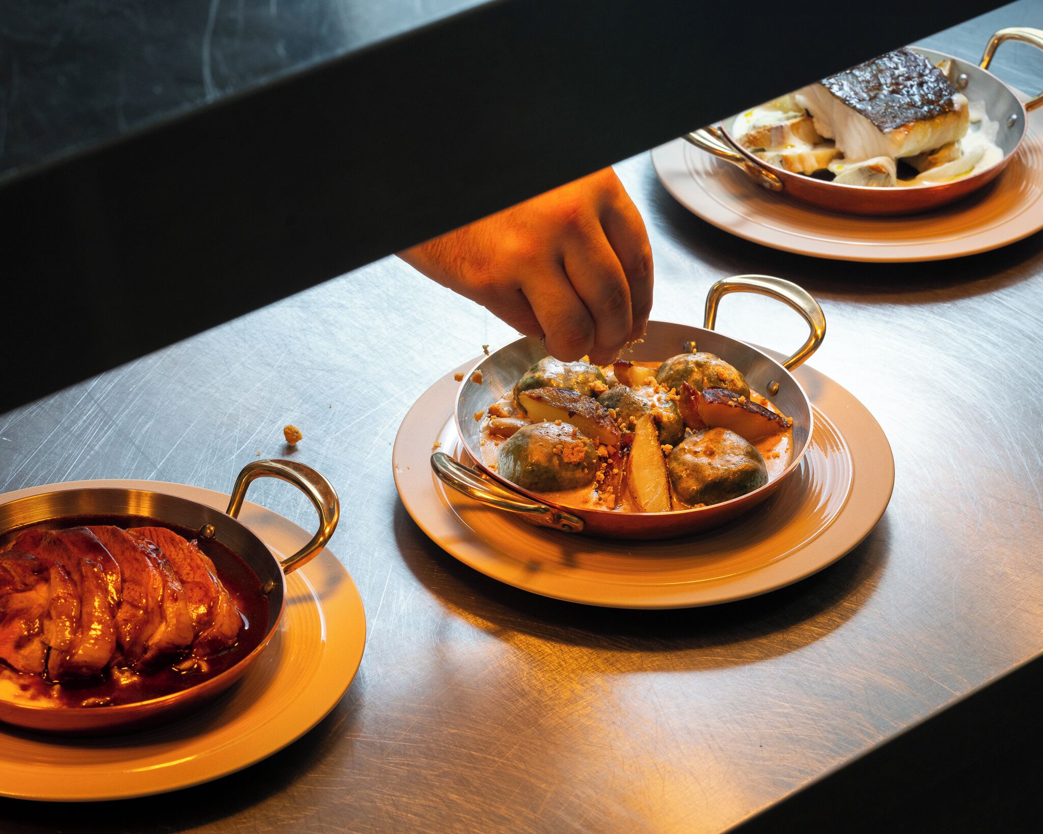A dining table with three dishes: a bowl of soup, a plate with meat, and a pan with vegetables.