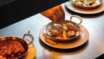 A dining table with three dishes: a bowl of soup, a plate with meat, and a pan with vegetables.