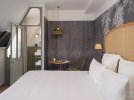A hotel room with a large bed, a small round table with a lamp, a chair, and a view of the outside through a door.