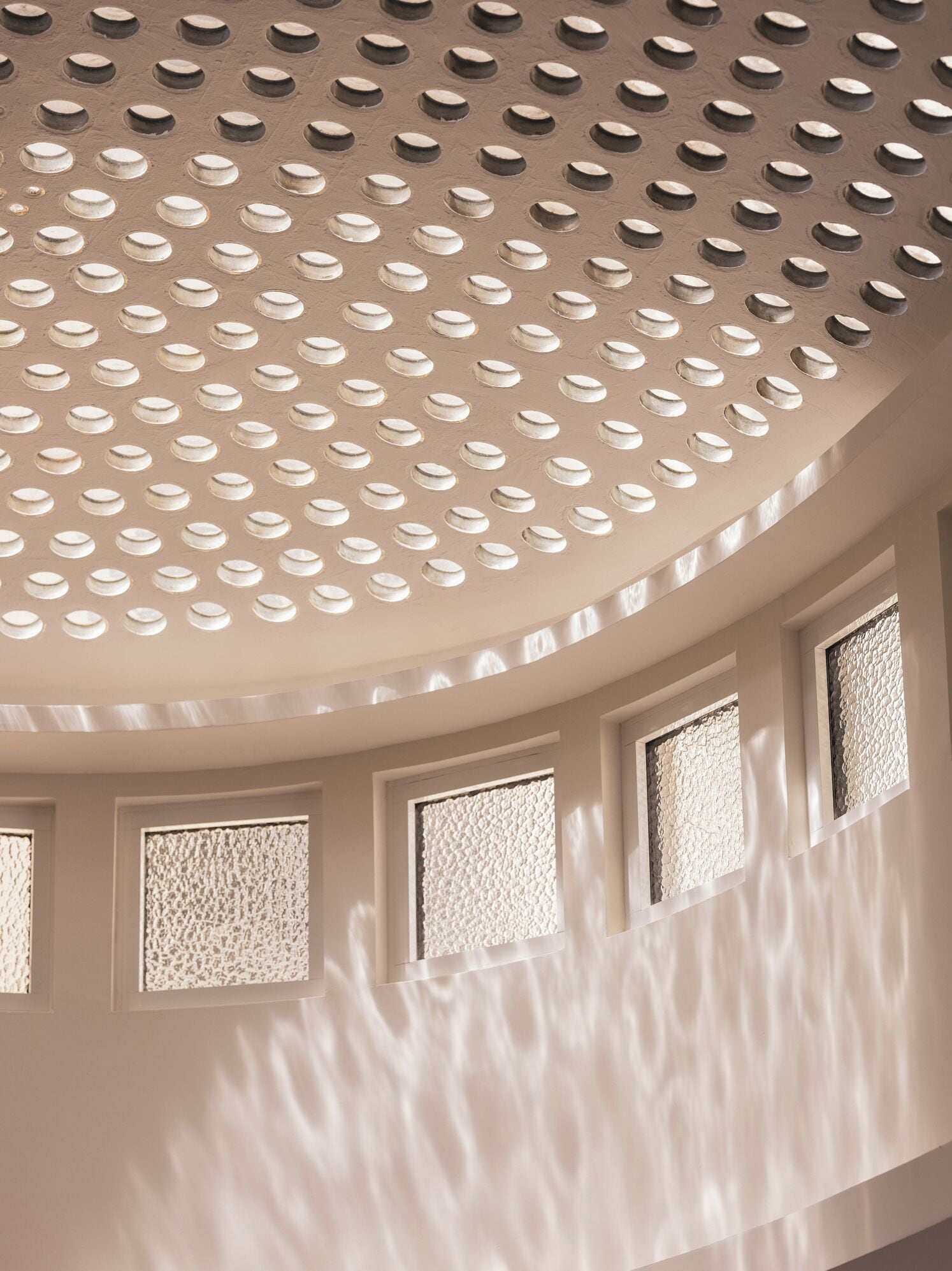 Un plafond orné de perforations circulaires et une série de fenêtres dotées de vitres texturées.
