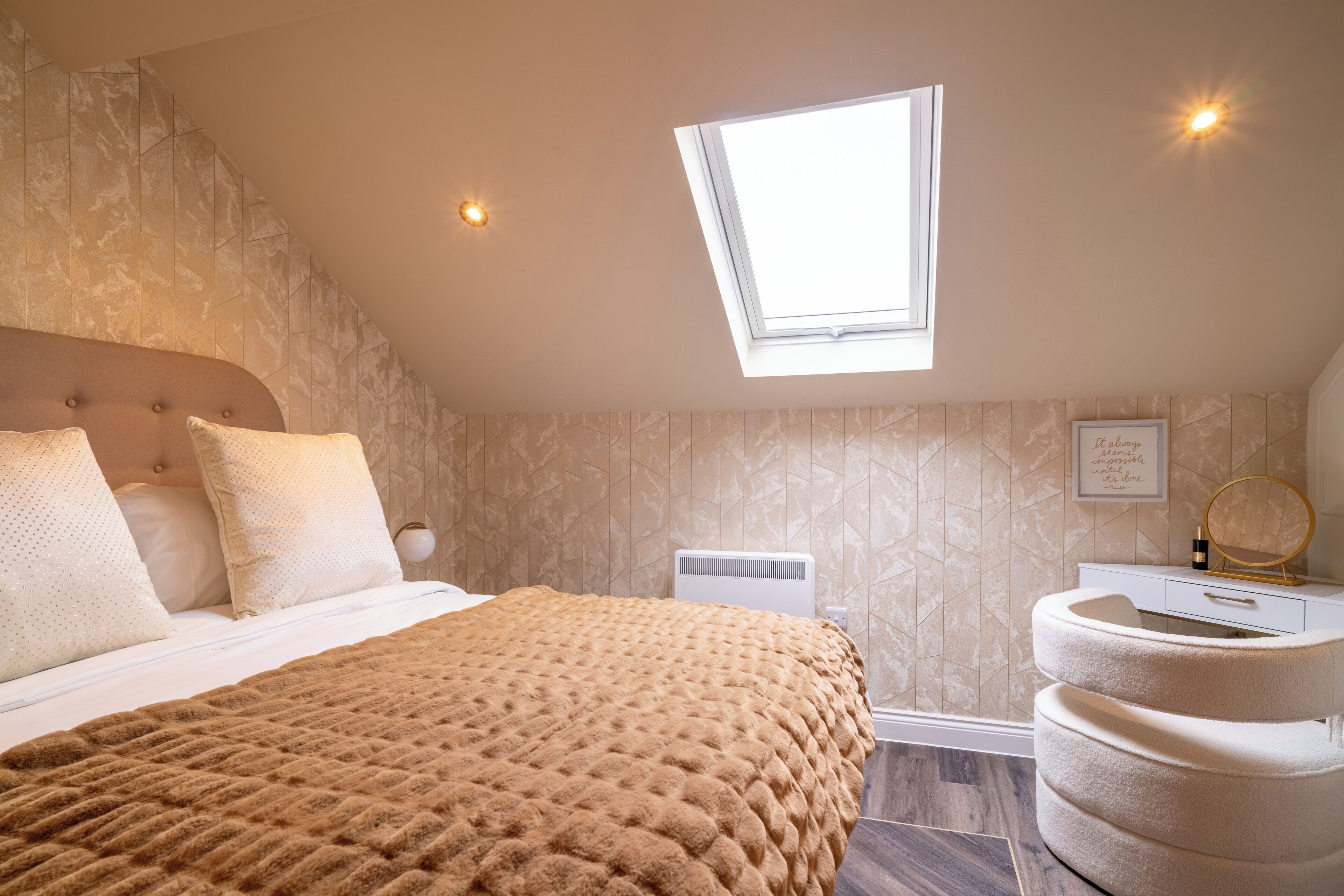 Un dormitorio con techo inclinado, tragaluz, cama con manta texturizada marrón, mesita de noche blanca con espejo y aire acondicionado montado en la pared.
