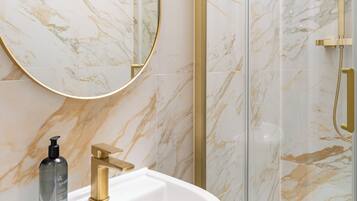 A bathroom with a white sink, gold faucet, and a glass-enclosed shower with gold fixtures.