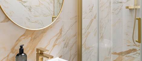 Une salle de bain avec un lavabo blanc, un robinet doré et une douche en verre avec des accessoires dorés.