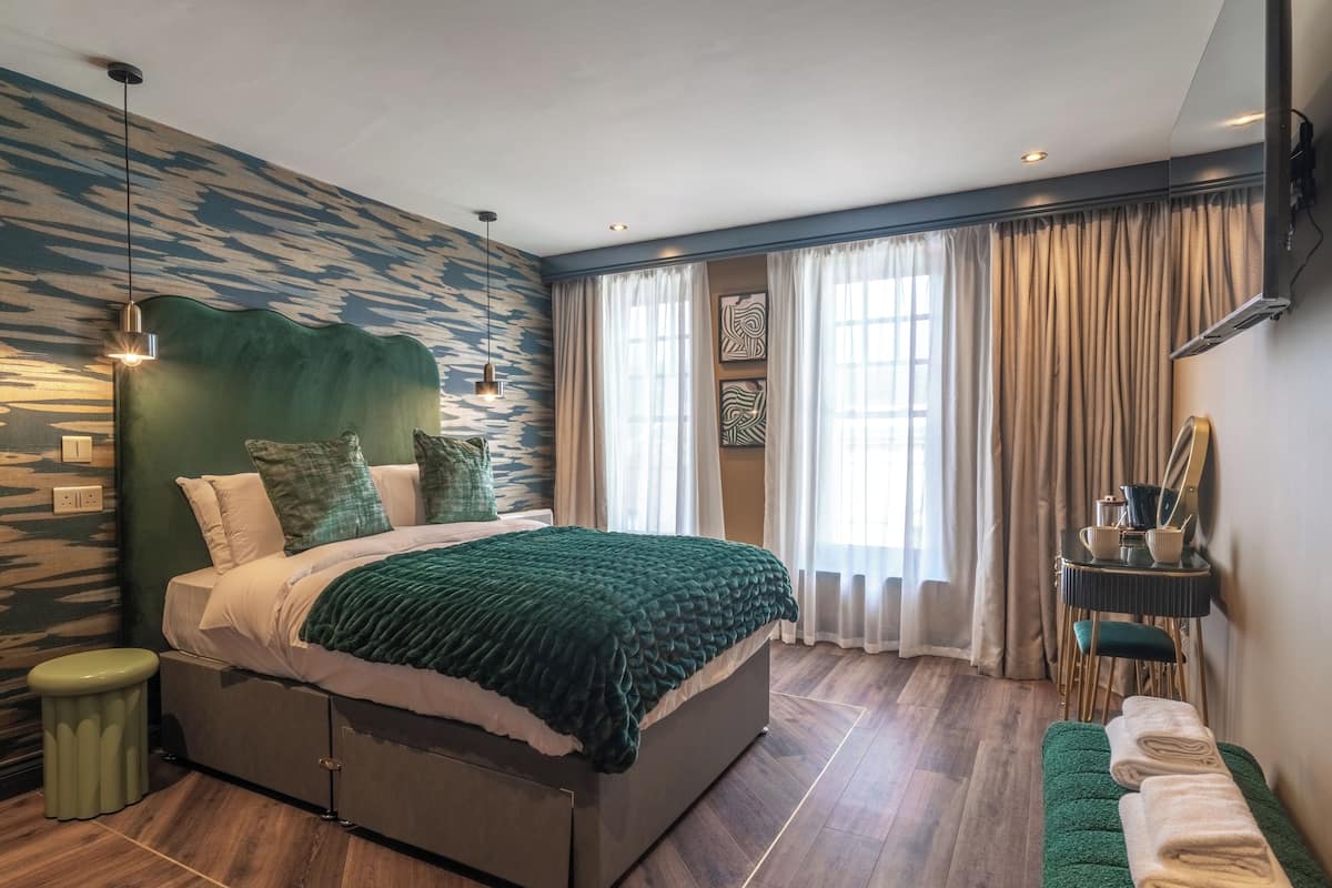 Un dormitorio moderno con una cama grande, una mesita de noche, un banco y vistas al exterior a través de amplias ventanas.