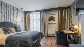 A modern bedroom with a bed, bedside table, and a desk with a lamp.