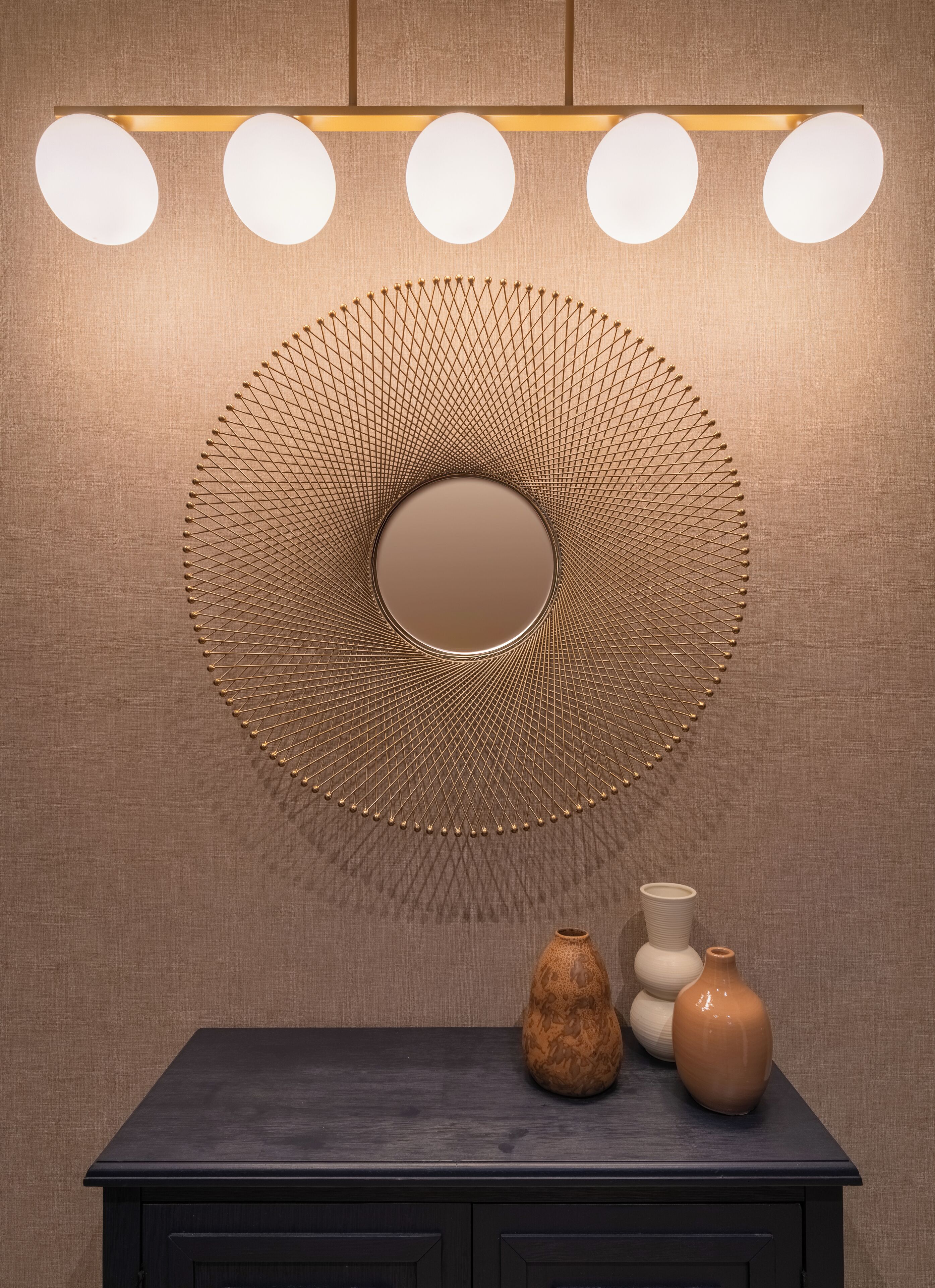 Un mur orné d’un élément décoratif circulaire, un luminaire et une petite table sur laquelle sont posés des vases.