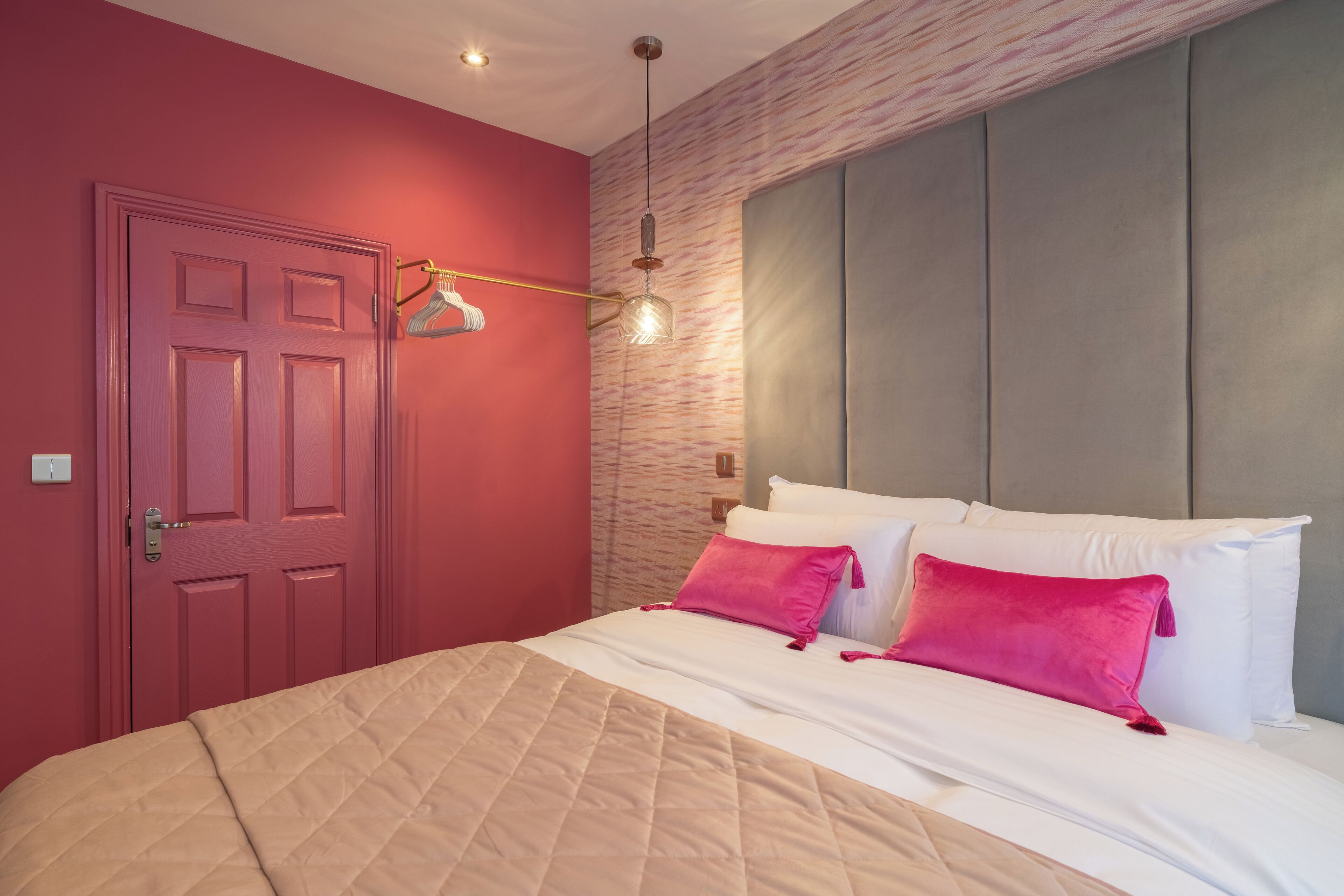 A bedroom with a red door, a bed with white and pink bedding, and a hanging light fixture.