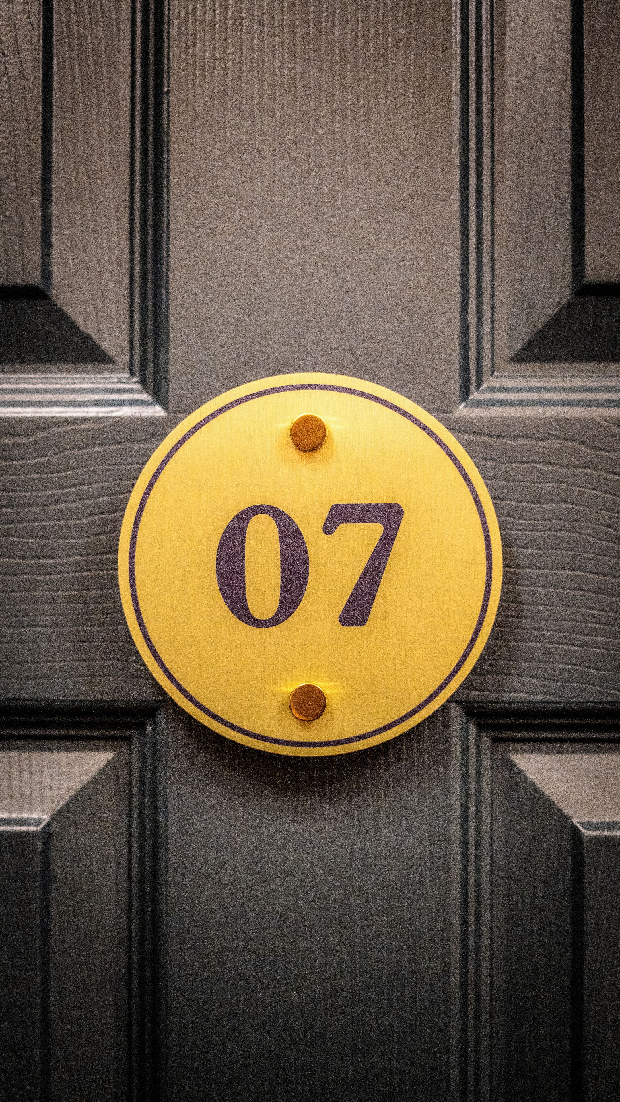 Une sonnette jaune avec le numéro 07, fixée sur une porte en bois sombre.