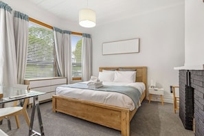A bedroom with a wooden bed, a desk with a chair, a fireplace, and a window with curtains. - Tranquil Haven in Ponsonby by Zodiak Stays (Auckland)