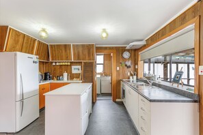 A compact kitchen with wooden cabinets, a refrigerator, a sink, and a clock on the wall. - Tranquil Haven in Ponsonby by Zodiak Stays (Auckland)