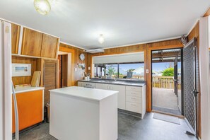 A compact kitchen with a central island, wooden paneling, and a view through an open door to the outside. - Tranquil Haven in Ponsonby by Zodiak Stays (Auckland)