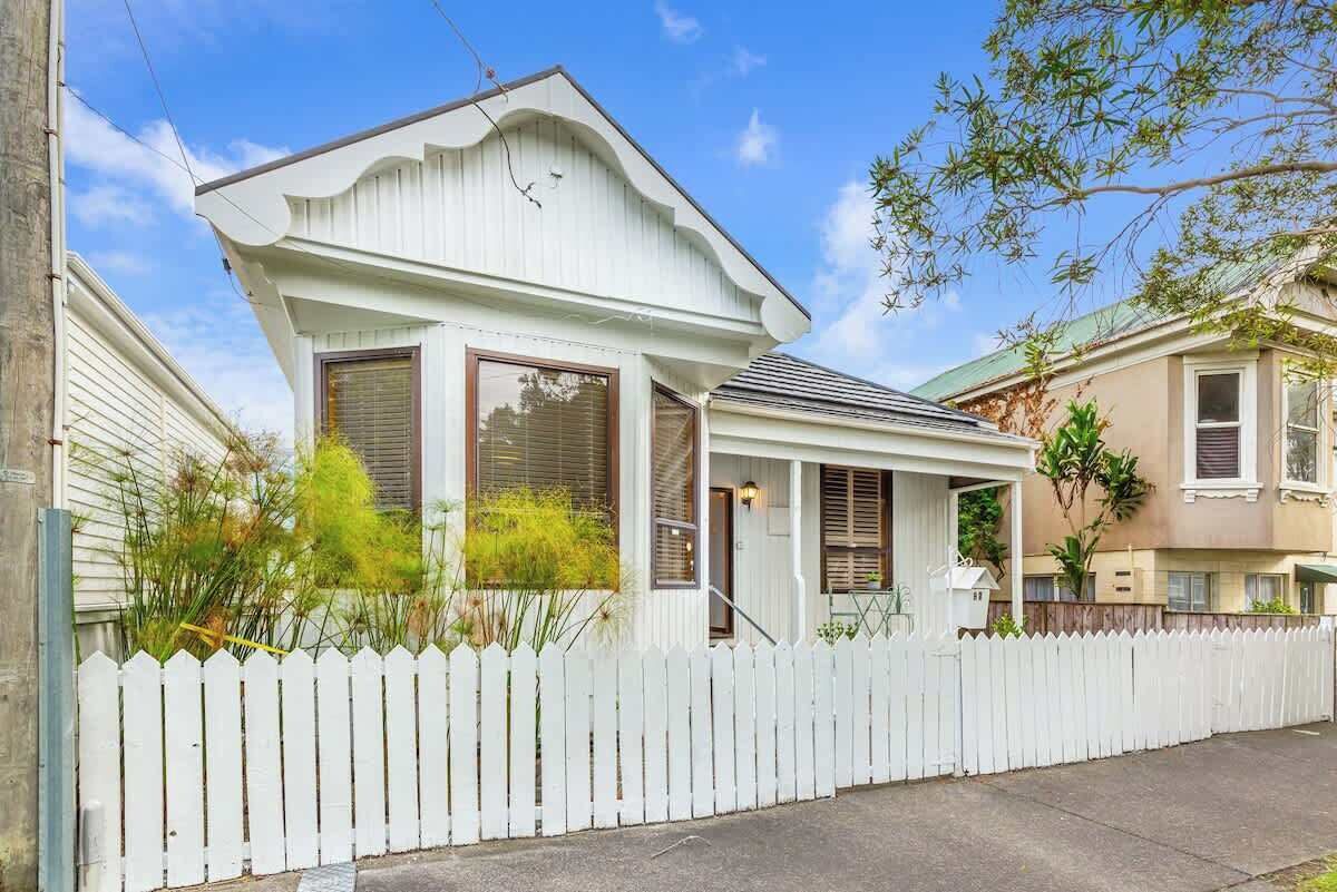 A single-story house with a white picket fence, a covered porch, and a front door.