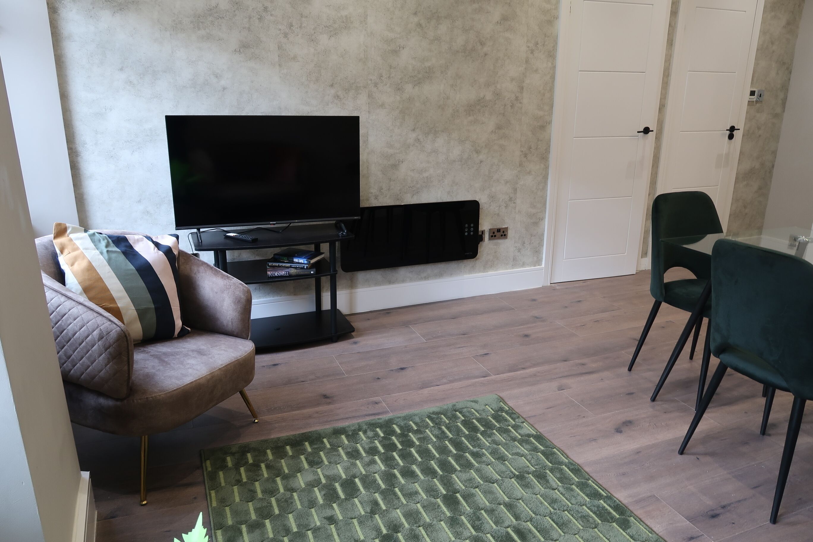 A living room with a flat-screen TV, a sofa, a green chair, and a patterned rug.