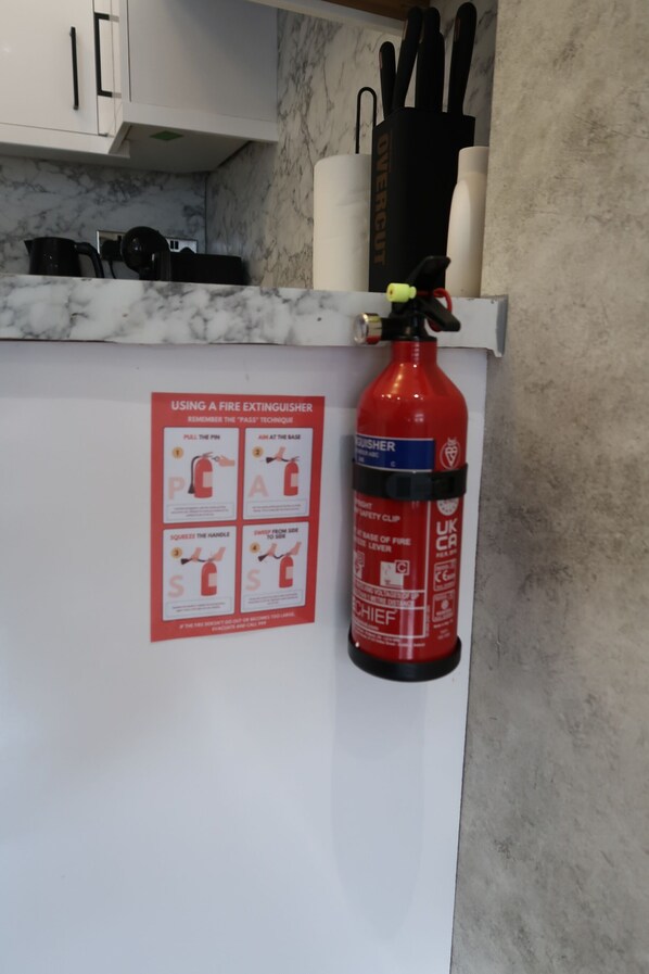 A kitchen with a fire extinguisher mounted on the wall, a knife block, and a poster with instructions on using a fire extinguisher.