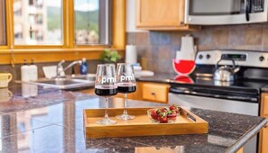 A kitchen with a granite countertop, a microwave, a stove, and a tray with two glasses of red wine and a bowl of strawberries.
