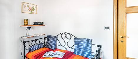 Une petite pièce avec un lit, une étagère sur laquelle se trouve une radio, une lampe et une porte.