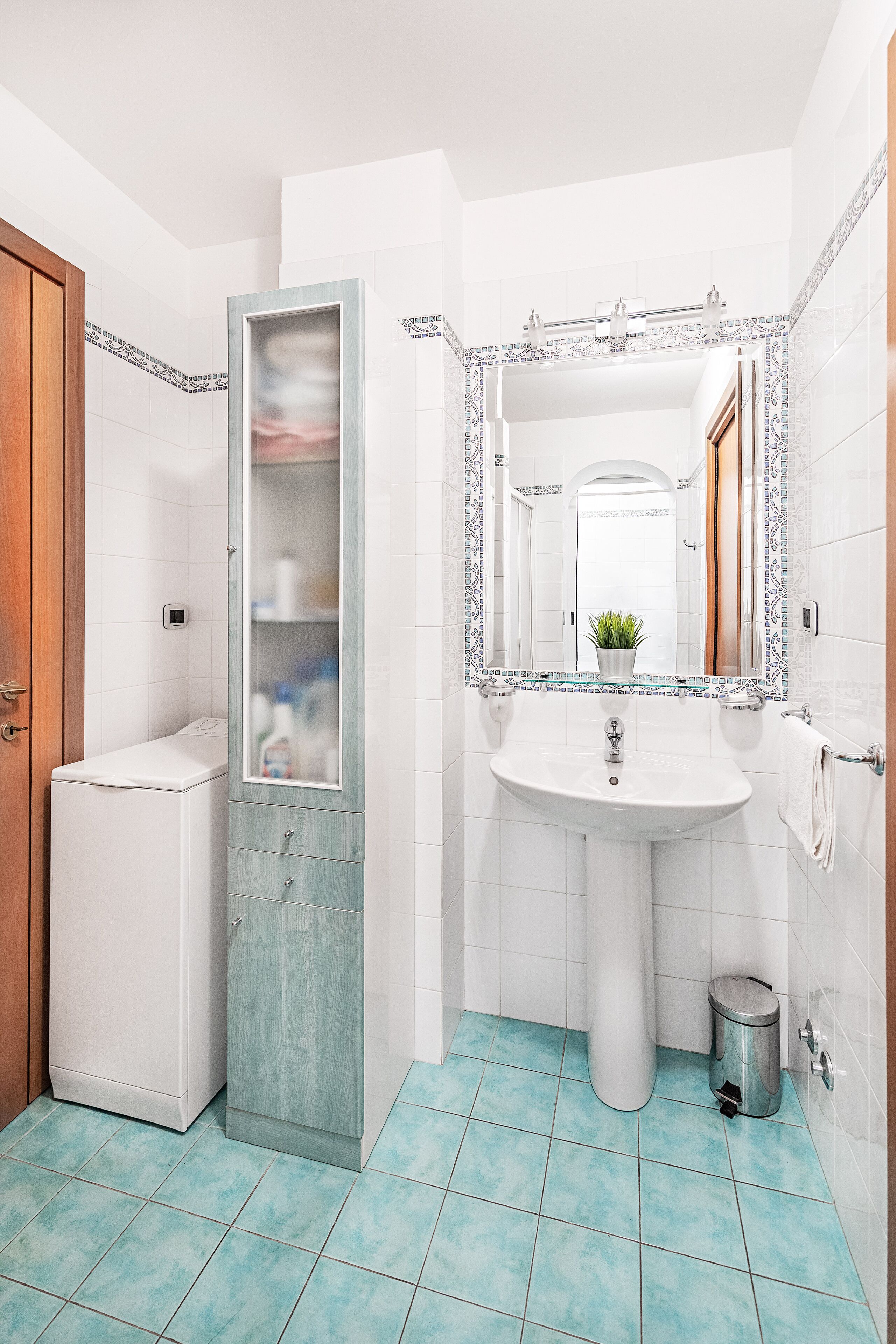Une salle de bain avec un lavabo blanc, un miroir doté d’un cadre décoratif, une petite plante en pot et des toilettes.