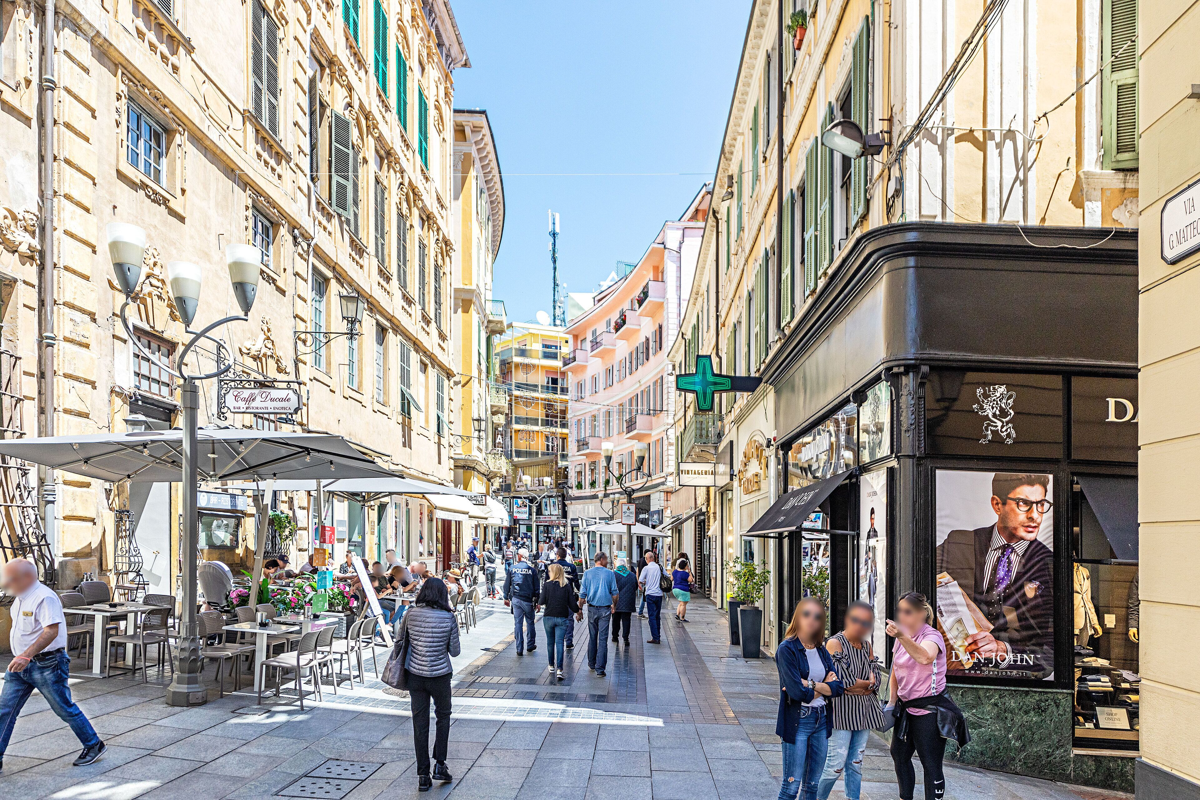 Una calle con cafés y tiendas, peatones y cielo despejado.