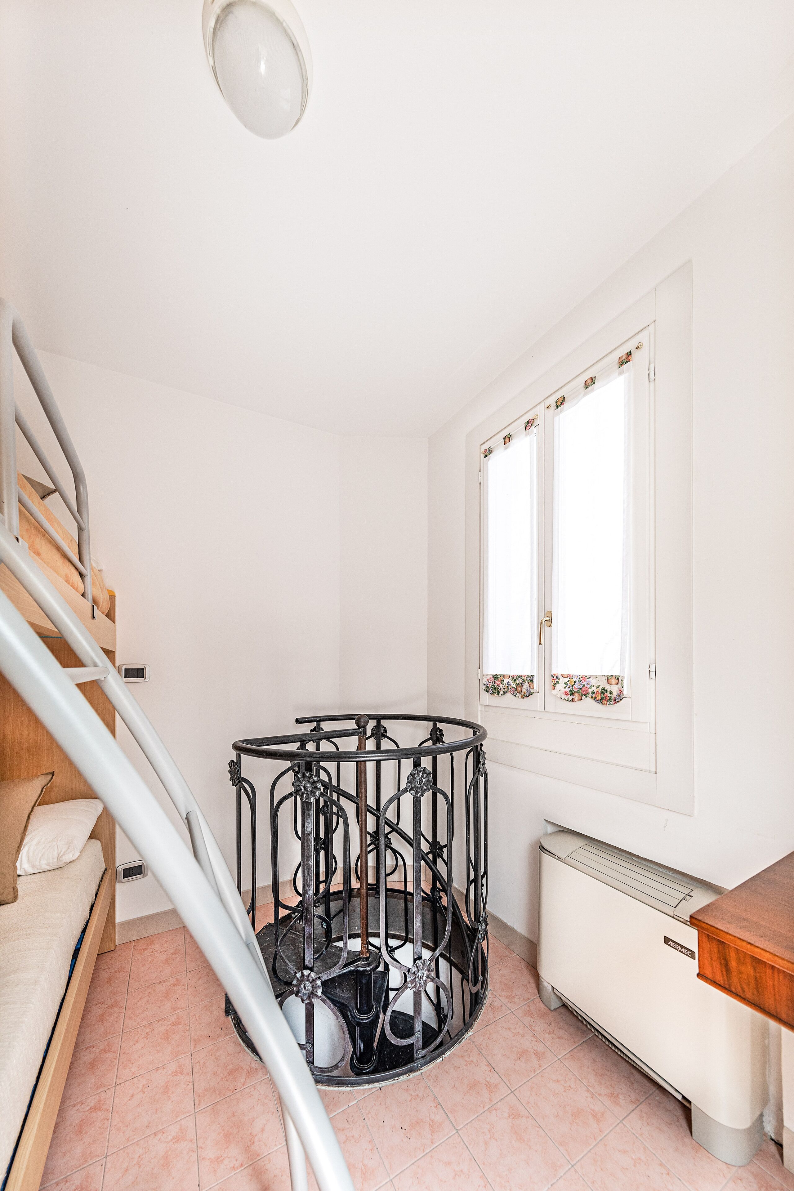A room with a bed, a radiator, a window with curtains, and a staircase.