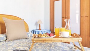 A neatly made bed with a patterned bedspread, a bedside table with a lamp, and a tray with breakfast items including pancakes, strawberries, and orange juice. - Gaudio Charming Apartment by Wonderful Italy (Sanremo)