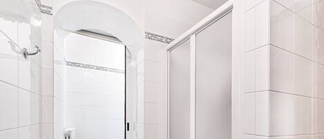 Une salle de bain avec des murs recouverts de carreaux blancs, une douche dotée d’une porte en verre et un sol carrelé de bleu.