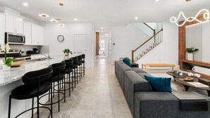 Una cocina moderna con una isla central, taburetes de bar y una zona de comedor con sofá y mesa de centro.