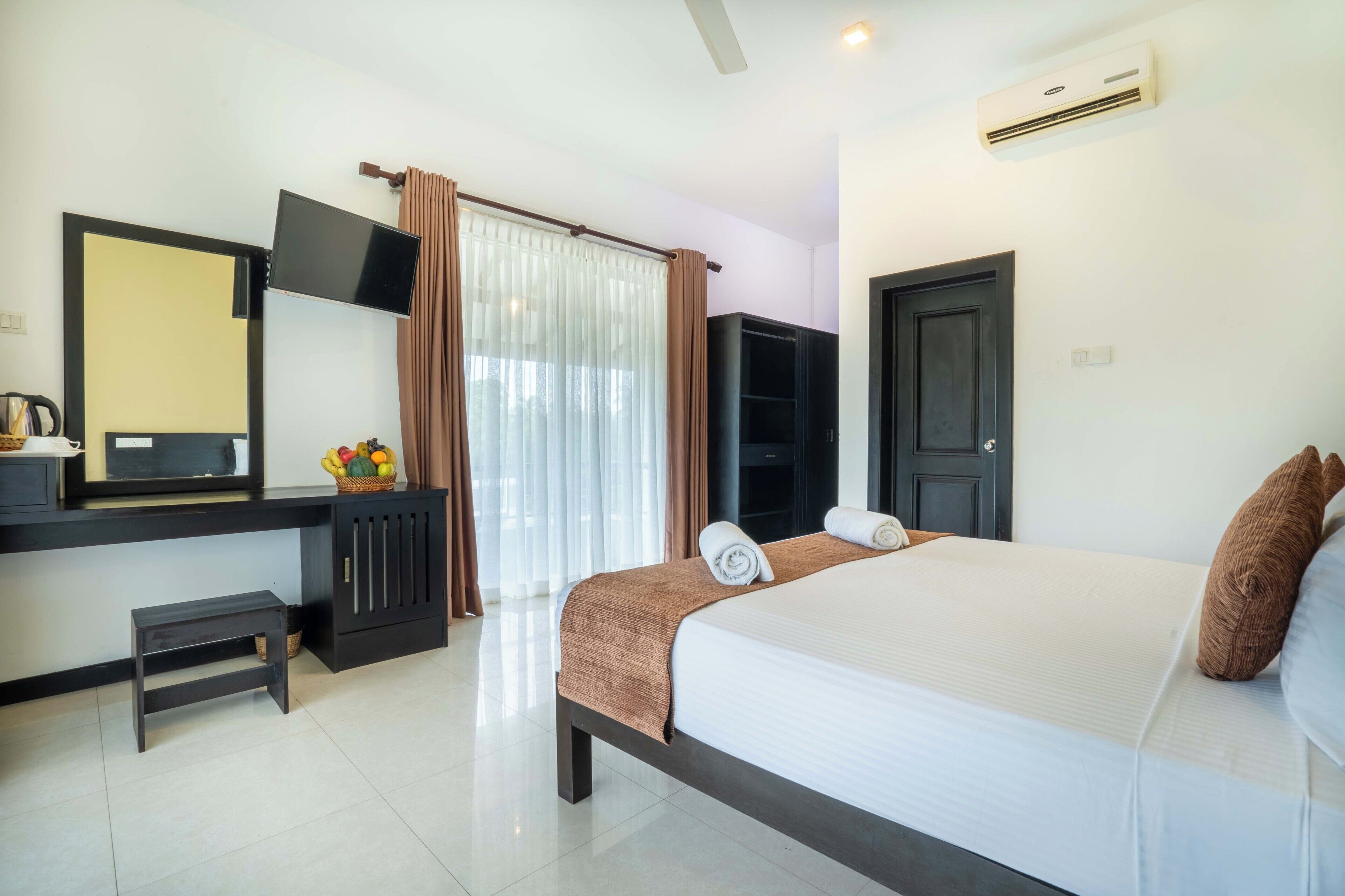 A hotel room with a bed, a desk with a flat-screen TV, a wardrobe, and a door.