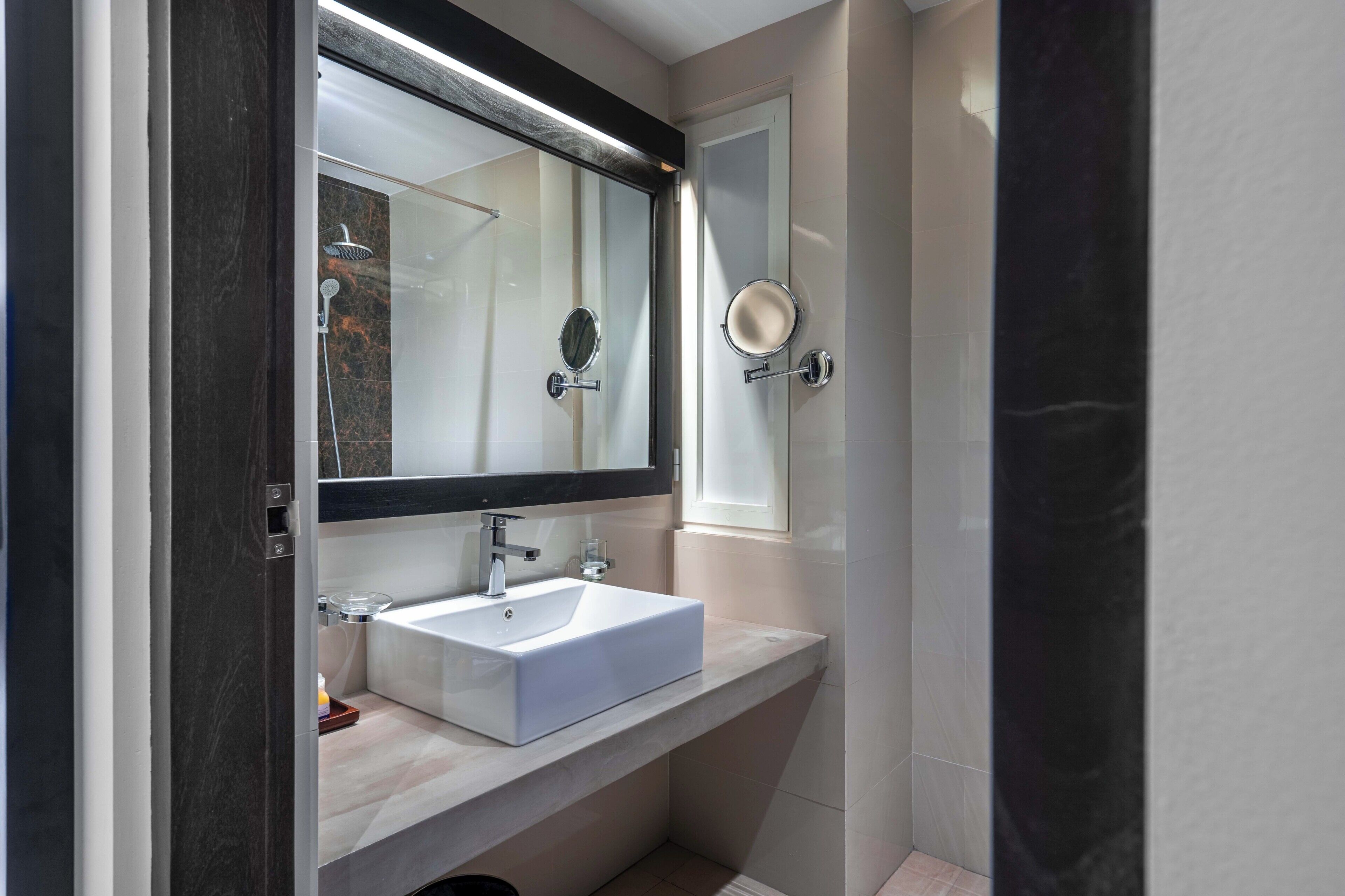 A modern bathroom with a white sink, a large mirror, and a shower.