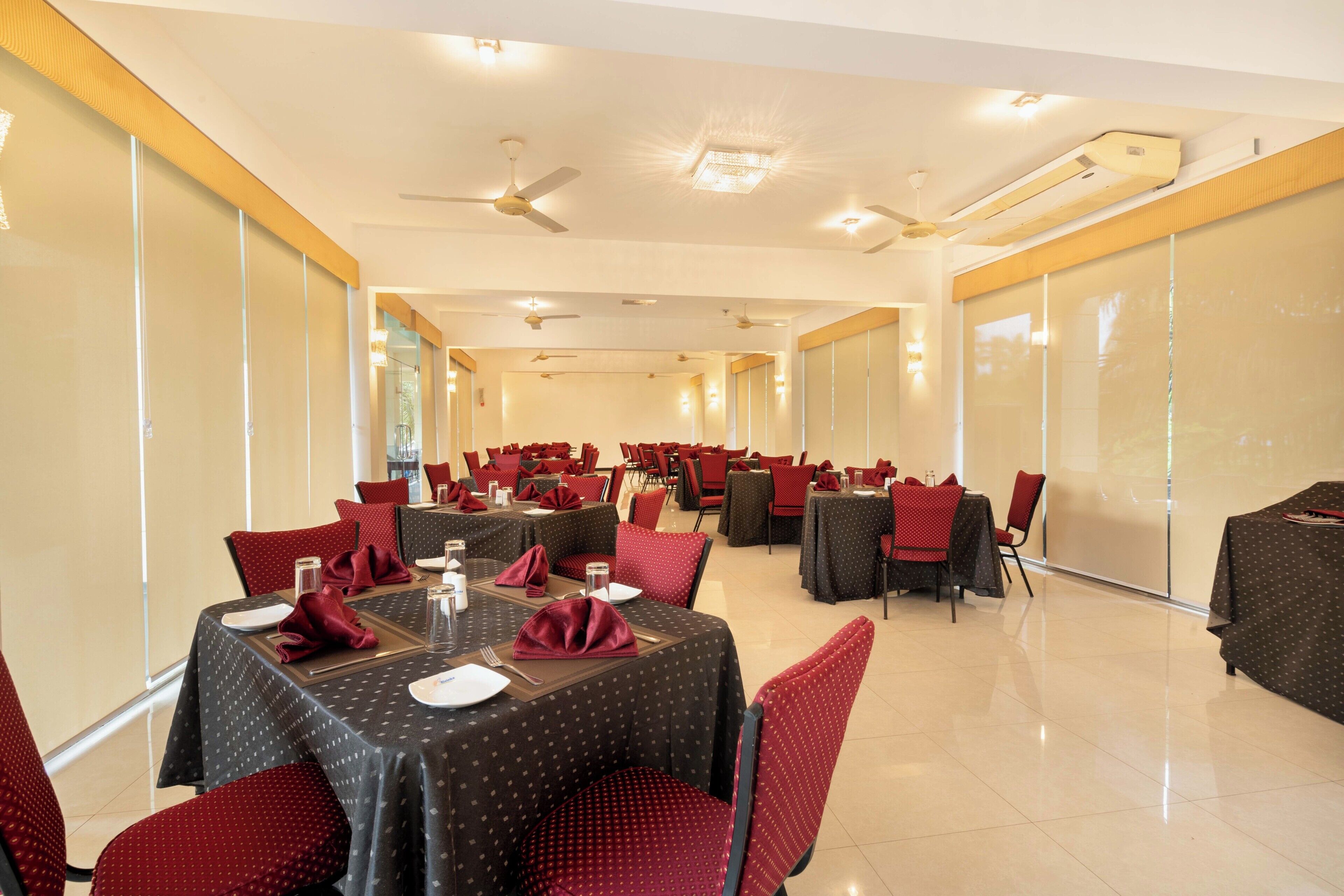 Un salón de conferencias con varias mesas y sillas, equipado con ventiladores de techo e iluminación empotrada.