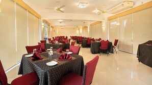 Un salón de conferencias con varias mesas y sillas, equipado con ventiladores de techo e iluminación empotrada.