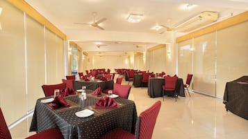 Un salón de conferencias con varias mesas y sillas, equipado con ventiladores de techo e iluminación empotrada.