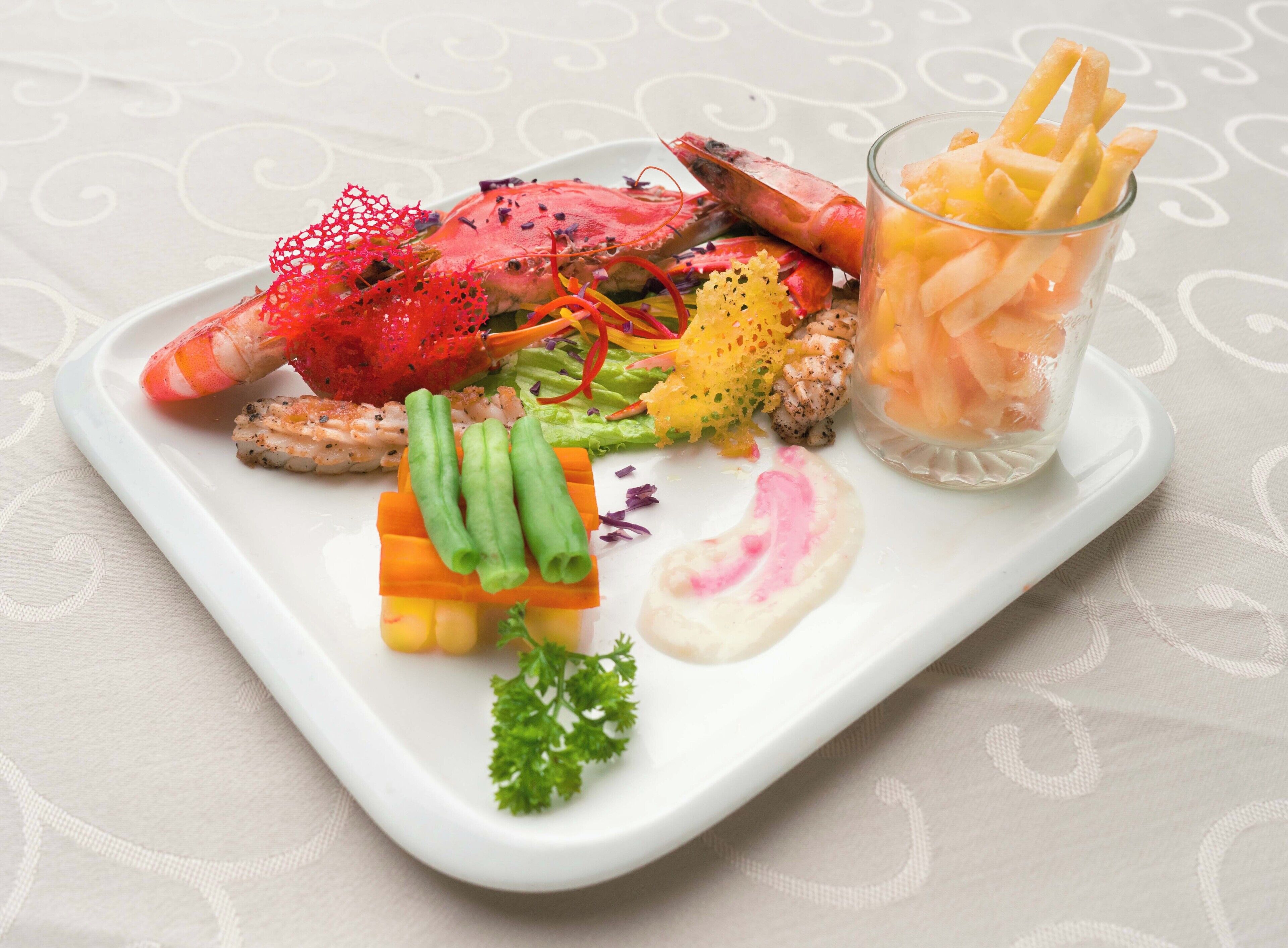 A white rectangular plate with a variety of food items including seafood, vegetables, and a glass of a clear beverage.
