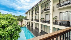 Un hotel de varios pisos con piscina, balcones y abundante vegetación.