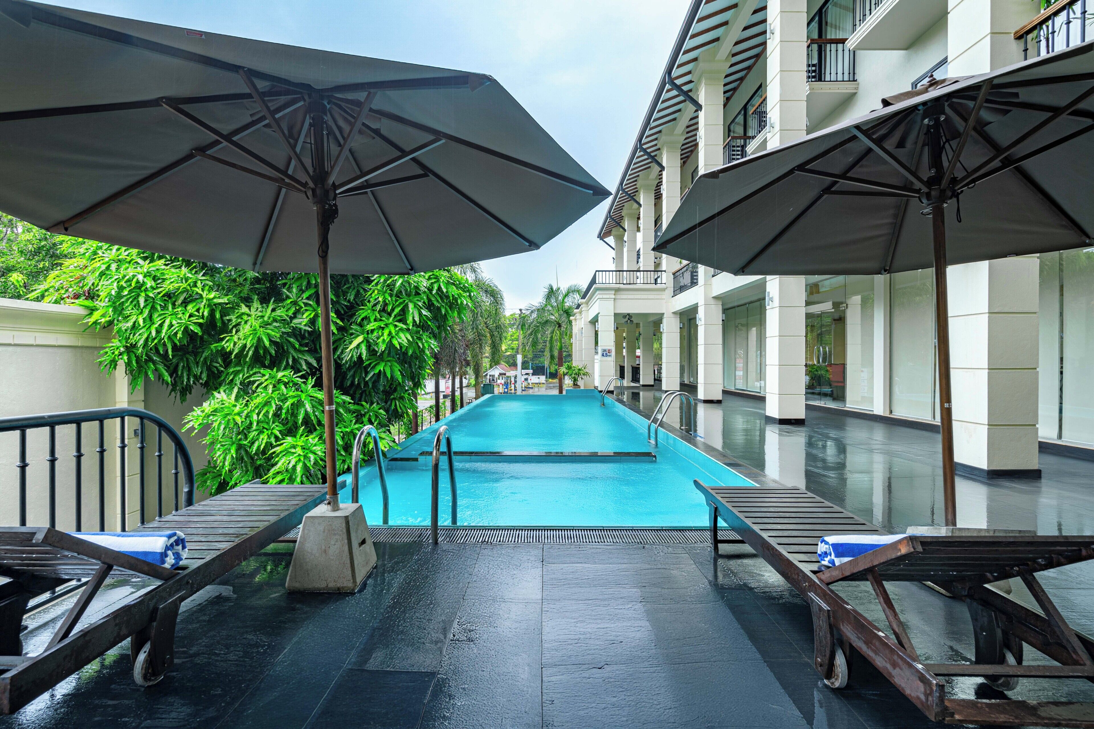 Un espace piscine équipé de parasols, de chaises longues et offrant une vue sur un immeuble doté de balcons.