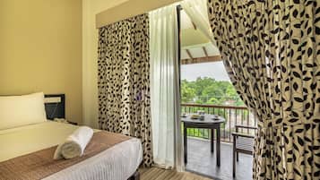 Habitación de hotel con cama, una mesita con juego de té y un balcón con vistas a zonas verdes.