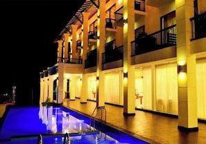 Un hotel con piscina, varios balcones e iluminación cálida.