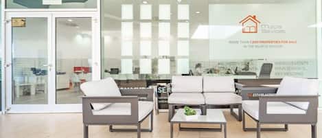 A modern interior with a reception desk, seating area, and glass doors leading outside.