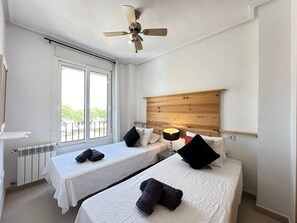 Habitación de hotel con dos camas, ventilador de techo, cabecero de madera y ventana con vista.