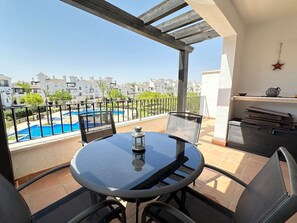 Un balcón con una mesa redonda y sillas, una piscina al fondo y una decoración con forma de estrella en la pared.