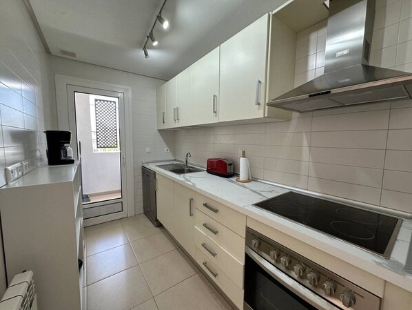 Una cocina con gabinetes blancos, una campana extractora de acero inoxidable, un lavamanos doble y un horno empotrado.