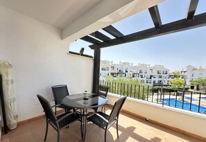 Un balcón con mesa y sillas, vista a una piscina y un complejo de edificios al fondo.