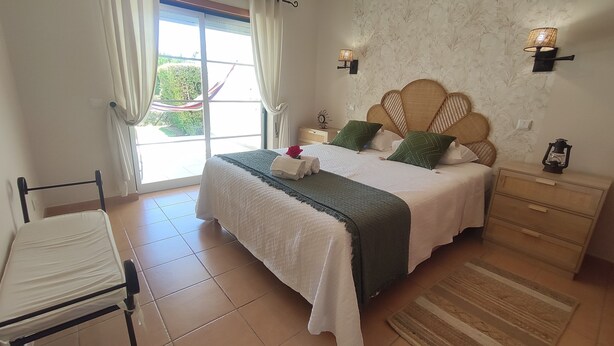 A neatly arranged bedroom with a bed, bedside tables, a chair, and a view through a window. - Sand, Sea and Salt - Alvor (Alvor)