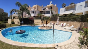A swimming pool with lounge chairs and umbrellas, surrounded by a landscaped garden and residential buildings. - Sand, Sea and Salt - Alvor (Alvor)