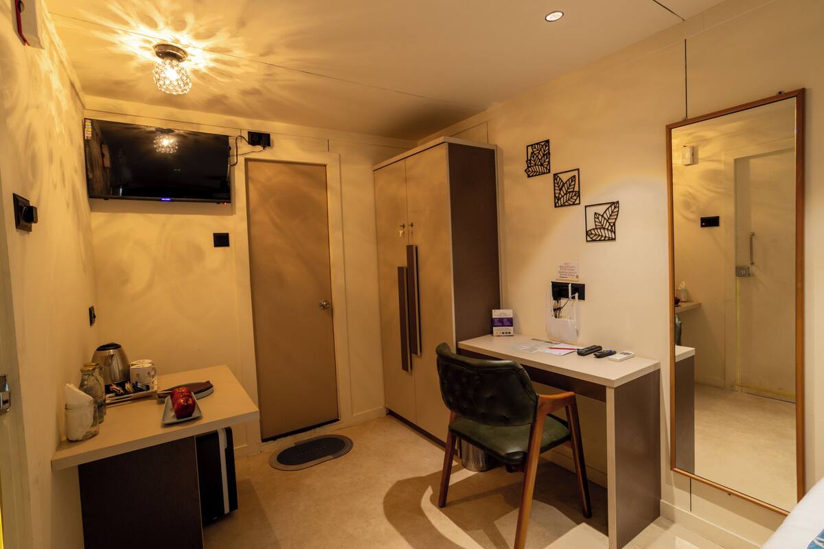 A compact hotel room with a desk, chair, and a large mirror.